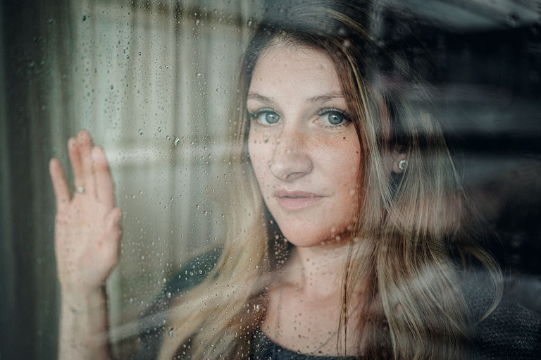 Portrait von Mädchen, die hinter einer Glaswand steht, die voller Regentropfen sind in Villach