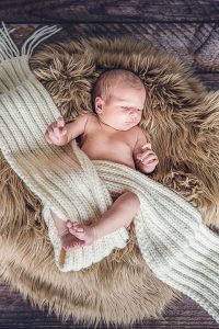 Newborn Homestory, Baby liegt in Schafsfell und Wollschal gewickelt in Villach