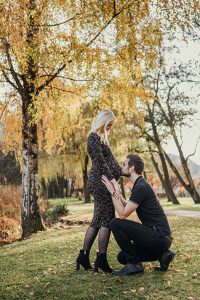 Mann kniet vor der Frau und küsst ihren Babybauch im Park von Pörtschach am Wörther See