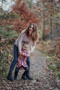 Mutter hält Tochter von hinten und sie lachen im Wald beim Forstsee