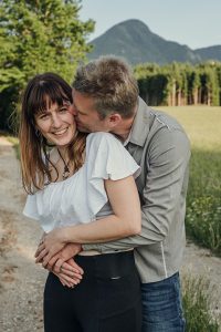 Mann umarmt seine Freundin und küsst sie auf die Wange auf einem Feldweg im Rosental
