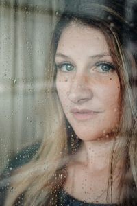 Portrait von Mädchen, die hinter einer Glaswand steht, die voller Regentropfen sind in Villach