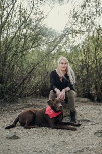 Frau sitzt neben ihrem Labradorhund Fin am Forstsee